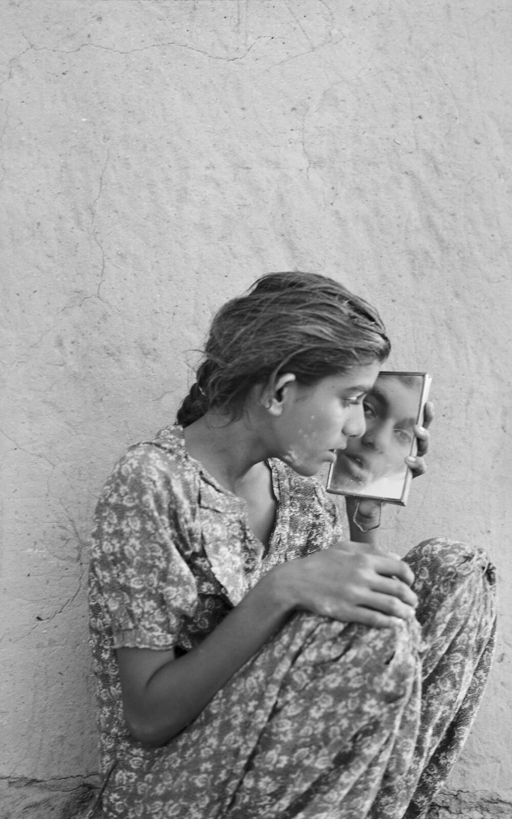 B/W image of a sitting young woman looking at herself in a mirror she holds in her left hand