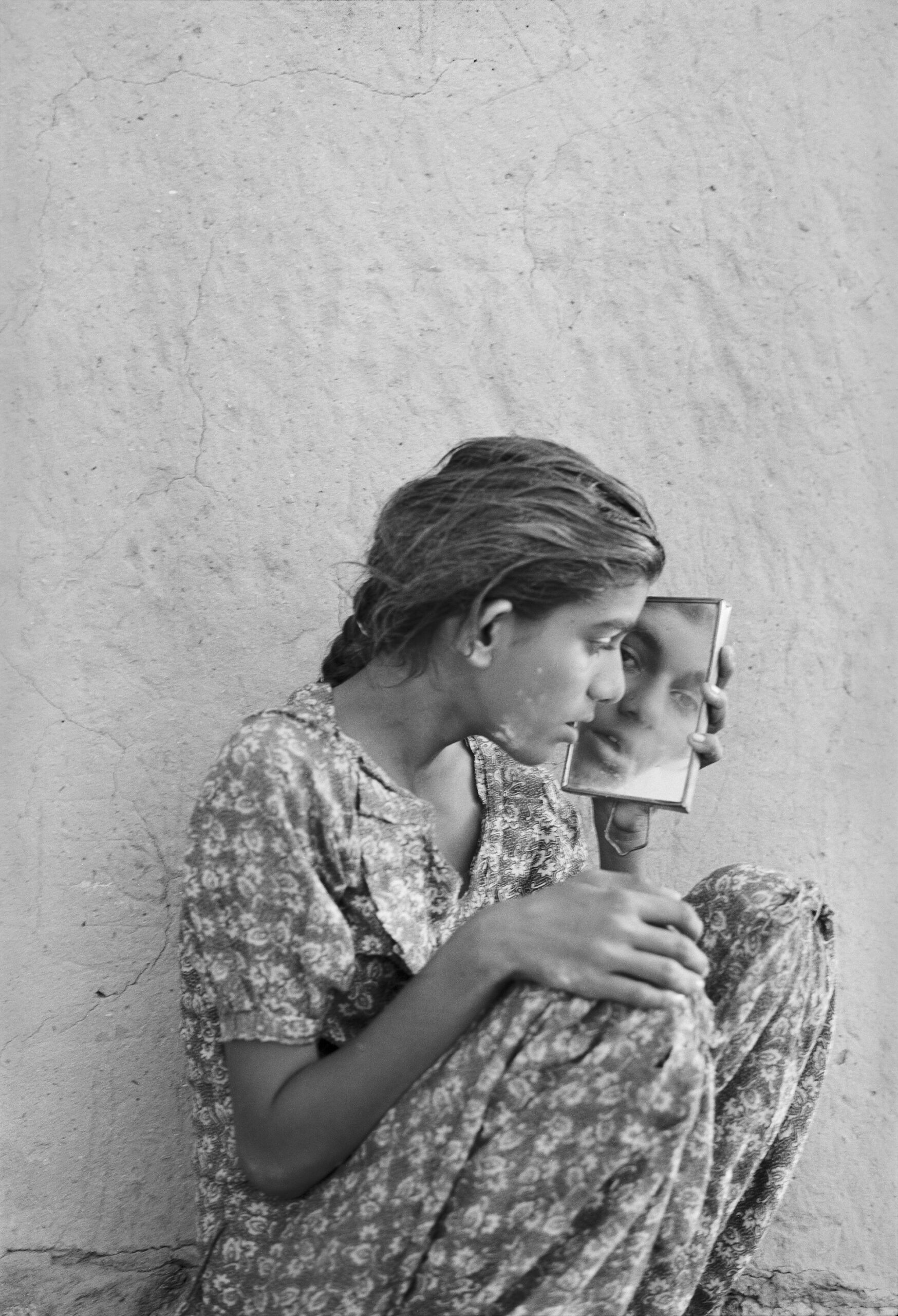 B/W image of a sitting young woman looking at herself in a mirror she holds in her left hand